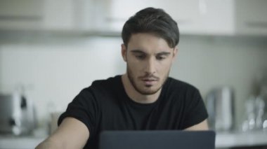 Ciddi bir adam evde çalışırken kahve içer. Dizüstü bilgisayar üzerinde çalışan odaklanmış iş adamı