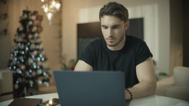 Um homem sério a falar ao telefone na casa de Natal. masculino cara trabalho no computador mesa — Vídeo de Stock