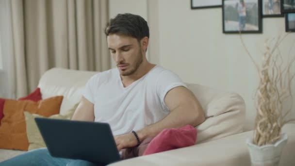 Занепокоєний бізнесмен працює на ноутбуці на дивані. Непростий чоловік — стокове відео