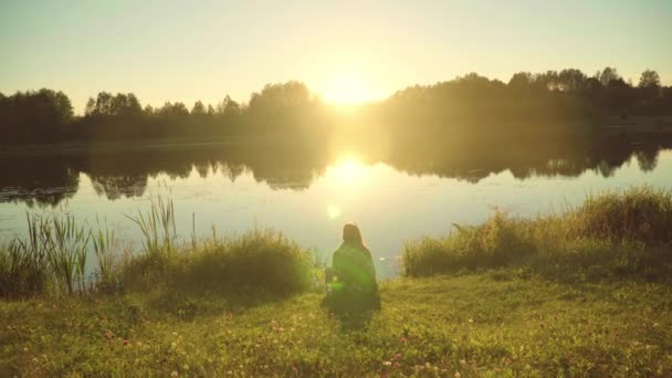 Lonely Girl insvept i pläd sitter på stranden av sjön och titta på soluppgången — Stockvideo