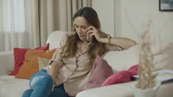 Щаслива жінка телефонує на диван вдома. усміхнена жінка розмовляє мобільним телефоном — стокове відео