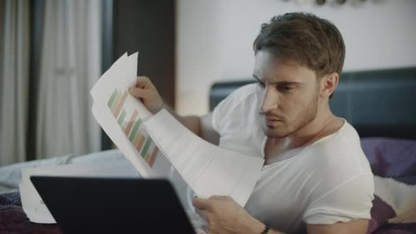 Seriöser Mann arbeitet nachts mit Dokumenten und Laptop auf Sofa — Stockvideo