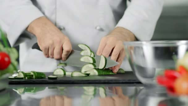 新鮮な野菜を切る男性シェフ。クローズアップシェフの手はキュウリをスライス. — ストック動画