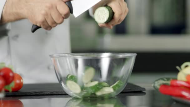 Шеф-повар режет свежий огурец в стеклянной чаше в замедленной съемке на кухне — стоковое видео