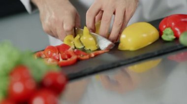 Erkek şef mutfak restoranında taze yemek pişiriyor. Yakın eller biber dilimleme