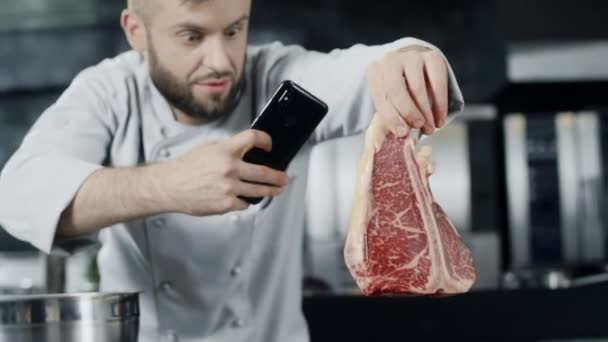 Chef haciendo foto de carne con teléfono móvil. Chef masculino tomando fotos de bistec . — Vídeo de stock