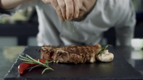 Соль повара жарит мясо на сковородке. Крупный план человек руки соленый стейк в замедленной съемке . — стоковое видео