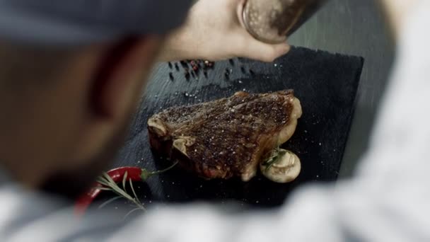 Chef pepering carne al tagliere di pietra. Uomo mani pepering striatura grigliato — Video Stock