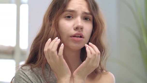 Незадоволена жінка торкається шкіри обличчя у дзеркалі ванної кімнати. Концепція проблемної шкіри — стокове відео