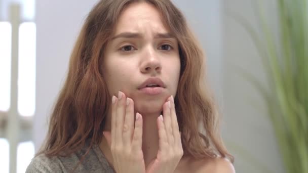 Olycklig ung kvinna tittar på ansiktet och röra huden främre badrumsspegel — Stockvideo