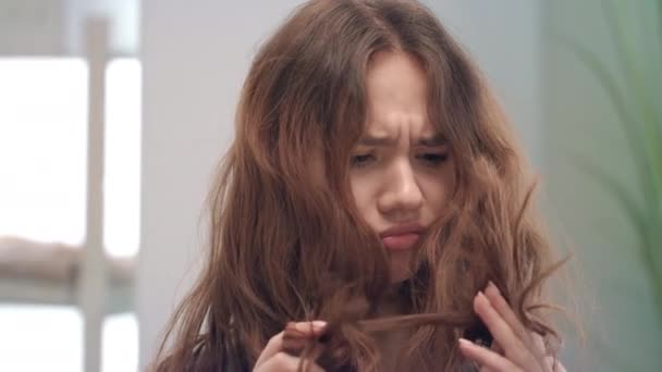 Olycklig ung kvinna röra och titta på torrt hår slutar i spegeln i badrummet — Stockvideo