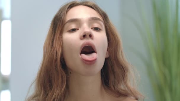 Mujer joven con la boca abierta mirando lengua y garganta en el espejo en el baño — Vídeos de Stock