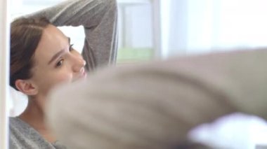 Mutlu kadın kıvırcık saçlarını sallıyor ve arka aynayı ev banyosunda yapıyor.