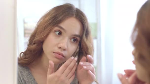Молодая женщина снимает контактные линзы для глаз перед зеркалом в домашней ванной комнате — стоковое видео