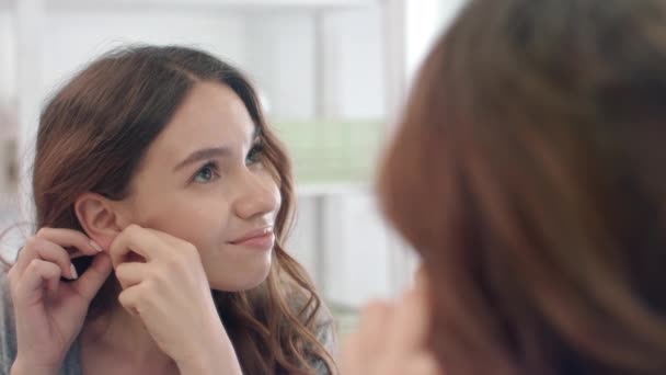 Upset woman taking off earrings from ear looking in bathroom mirror — Stock Video