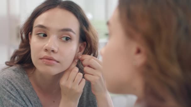 Vrolijke vrouw zetten oorbellen naar oor op zoek in badkamer spiegel thuis — Stockvideo