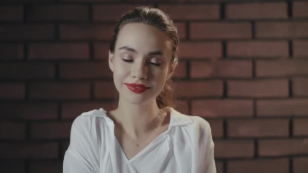 Érzéki nő harapás piros ajkak és belenéz kamera téglafal háttér — Stock videók