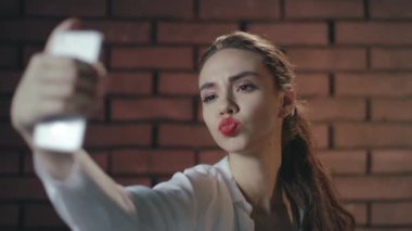 Tuğla duvardaki fotografta cep telefonu kullanan seksi kadın.