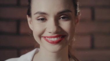 Güzel bir kadın gülümsüyor ve duvardaki kameraya bakıyor.