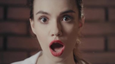 Şok olmuş bir kadın, ağzı açık ve gözleri önde, duvarın arkasında..