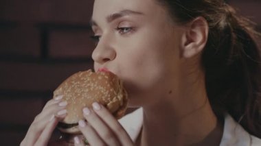 Fast food kafenin duvarında hamburger yiyen aç bir kadın.
