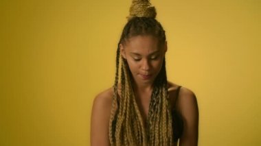 Stüdyoda sarı arka plan üzerinde afro saç modeli twirling el ile şaşkın kadın
