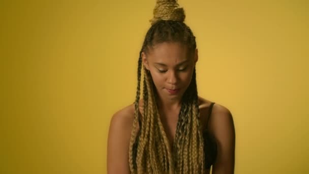 Confused woman with afro hairstyle twirling hand on yellow background in studio — Stock Video