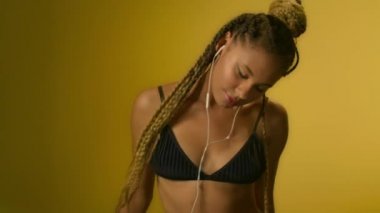 Sarı arka planda kulaklıkla cep telefonuyla müzik dinleyen dans eden kadın