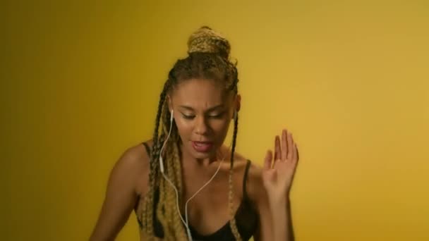 Chica africana escuchando música en el teléfono móvil en la pared amarilla. Afro chica bailando — Vídeos de Stock