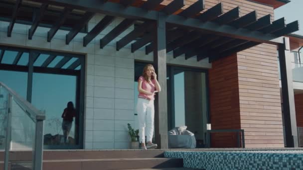 Reiche Frau spricht mobil auf der Veranda des Luxushauses. Reicher Eigentümer in der Nähe von Immobilien — Stockvideo