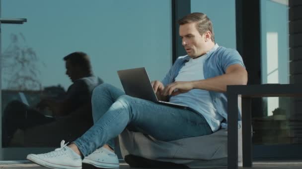 Расстроенный человек работает над ноутбуком. Беспокойный специалист сидит с ноутбуком на открытом воздухе — стоковое видео