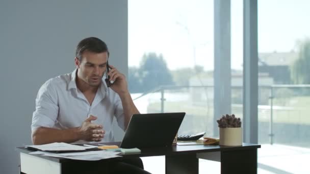 Επιχειρηματικός άνθρωπος που δουλεύει σε φορητό υπολογιστή. Συγκεντρωμένη άνθρωπος μιλά κινητό τηλέφωνο. — Αρχείο Βίντεο