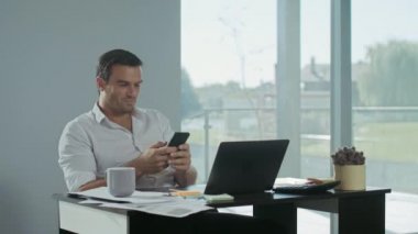 İş adamı iş yerinde cep telefonu kaydırma. Gülen adam mola veriyor.