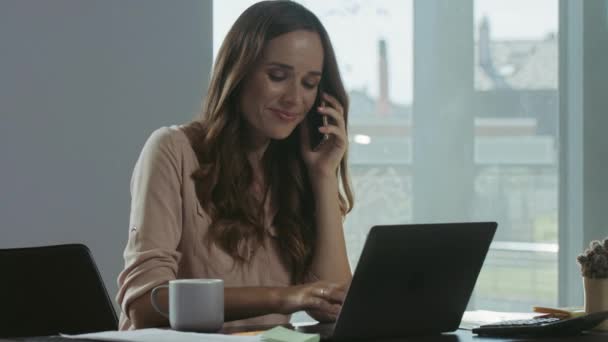 Een jonge vrouw die aan een laptop werkt. Portret van een lachende dame die mobiele telefoon chat — Stockvideo