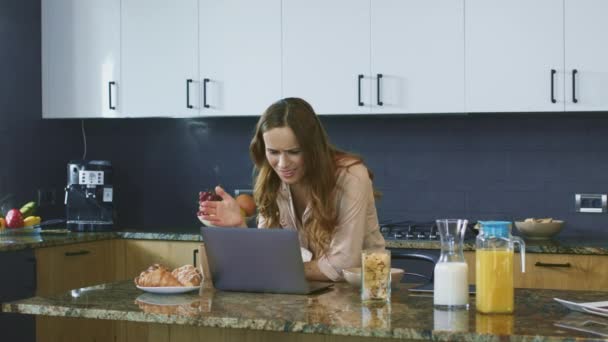 Obchodní žena kouká na video v kuchyni. Překvapený uživatel s pohledem na notebook. — Stock video