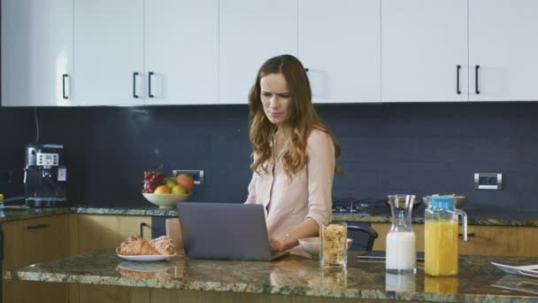 Mujer feliz viendo vídeo de pie en la cocina. Persona sonriente desplazamiento portátil . — Vídeos de Stock