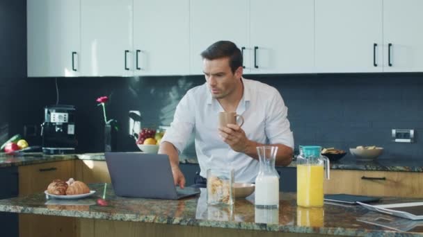 Um homem sorridente a ver um vídeo na cozinha. Computador de rolagem de pessoa feliz . — Vídeo de Stock