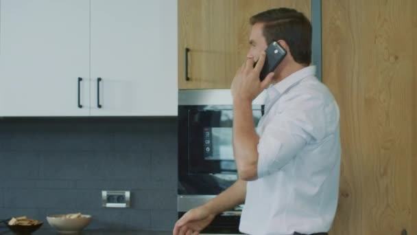 Üzleti ember beszél mobiltelefonján a konyhában. Az ember, akinek telefonhívást házban. — Stock videók