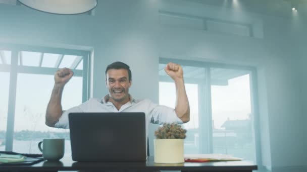Hombre de negocios feliz recibiendo buenas noticias en el ordenador portátil en el lugar de trabajo remoto — Vídeo de stock
