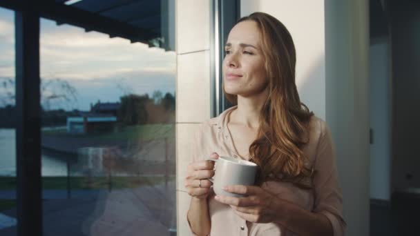 Entspannte Frau, die nach dem Arbeitstag in der Nähe des Fensters bleibt. hübsche Dame beobachtet Sonnenuntergang — Stockvideo