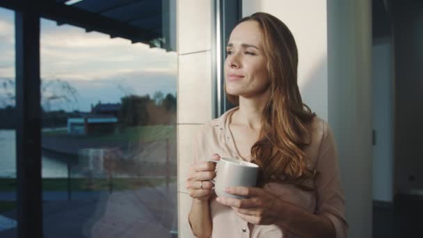 Avslappnad kvinna vistas nära fönster efter arbetsdag. Pretty Lady tittar på solnedgången — Stockvideo