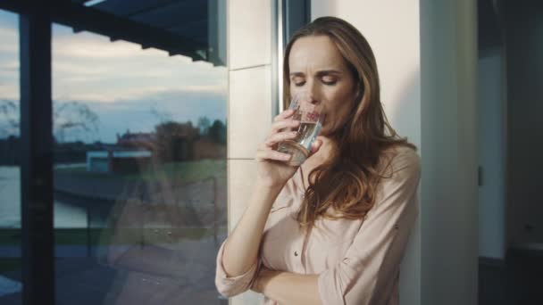 Χαλαρή γυναίκα πόσιμο νερό κοντά σε πανοραμικό παράθυρο. Διψασμένη κυρία πόσιμο νερό — Αρχείο Βίντεο