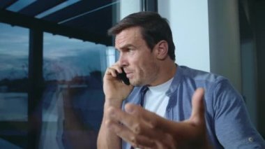 Pencerenin yanında mobil konuşan iş adamı. Sinirli adam konumunu açıklıyor.