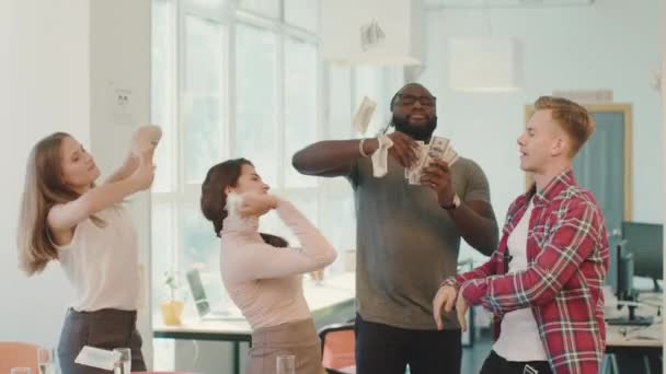 Jovens que fazem chuva com dinheiro no espaço de coworking. Dinheiro voando no ar . — Vídeo de Stock