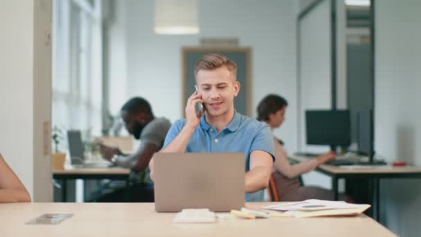 Młody człowiek rozmawia telefon komórkowy w biurze. Uśmiechnięty facet mówi na telefon — Wideo stockowe