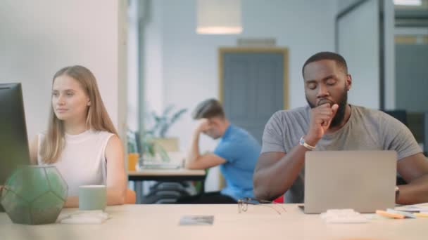 Hombre negro bostezando en el lugar de trabajo. Hombre cansado apoyando la cabeza sentado cerca del cuaderno . — Vídeos de Stock