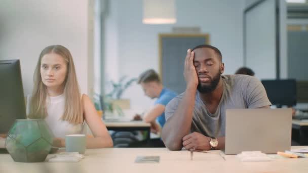 Vermoeide kerel in slaap vallen met laptop. Collega het geven van koffie aan slaperig man. — Stockvideo