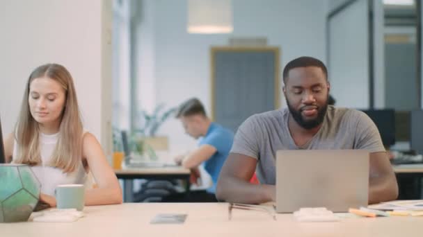 Afrikaner, der bei Coworking am Laptop arbeitet. freudiger Mann blickt Kamera an — Stockvideo