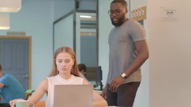 Mujer de negocios trabajando en cuaderno en coworking. negro hombre tratando de hacer masaje . — Vídeos de Stock