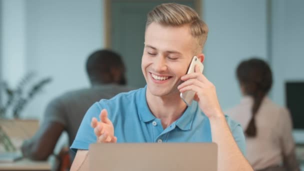Молодой человек говорит по телефону на рабочем месте. Портрет блондина, говорящего неофициально — стоковое видео